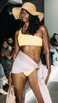 a black woman in a yellow bikini and hat on the runway